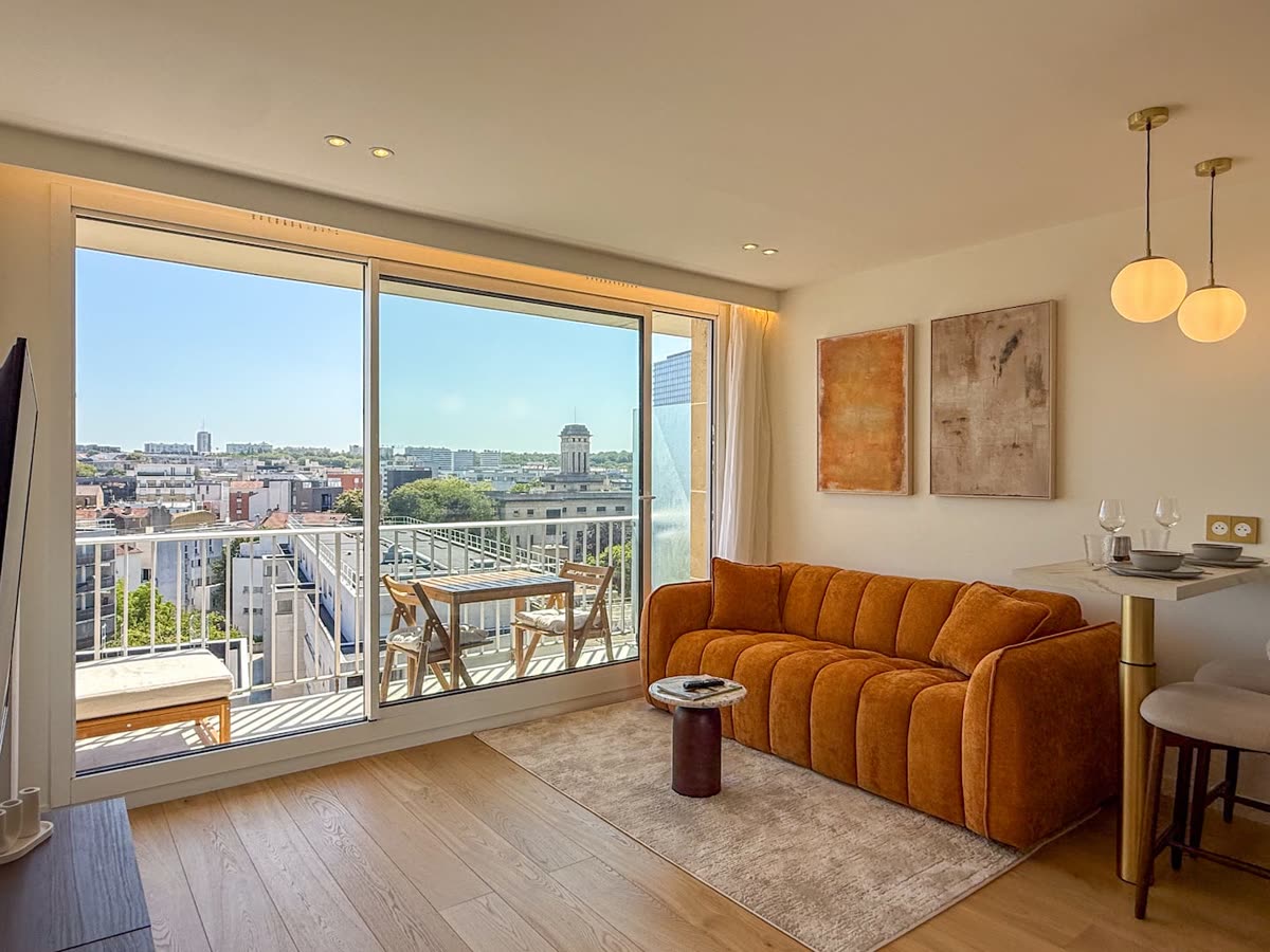 Listing photo of the living room: orange sofa, sliding door to a balcony with a view over the city